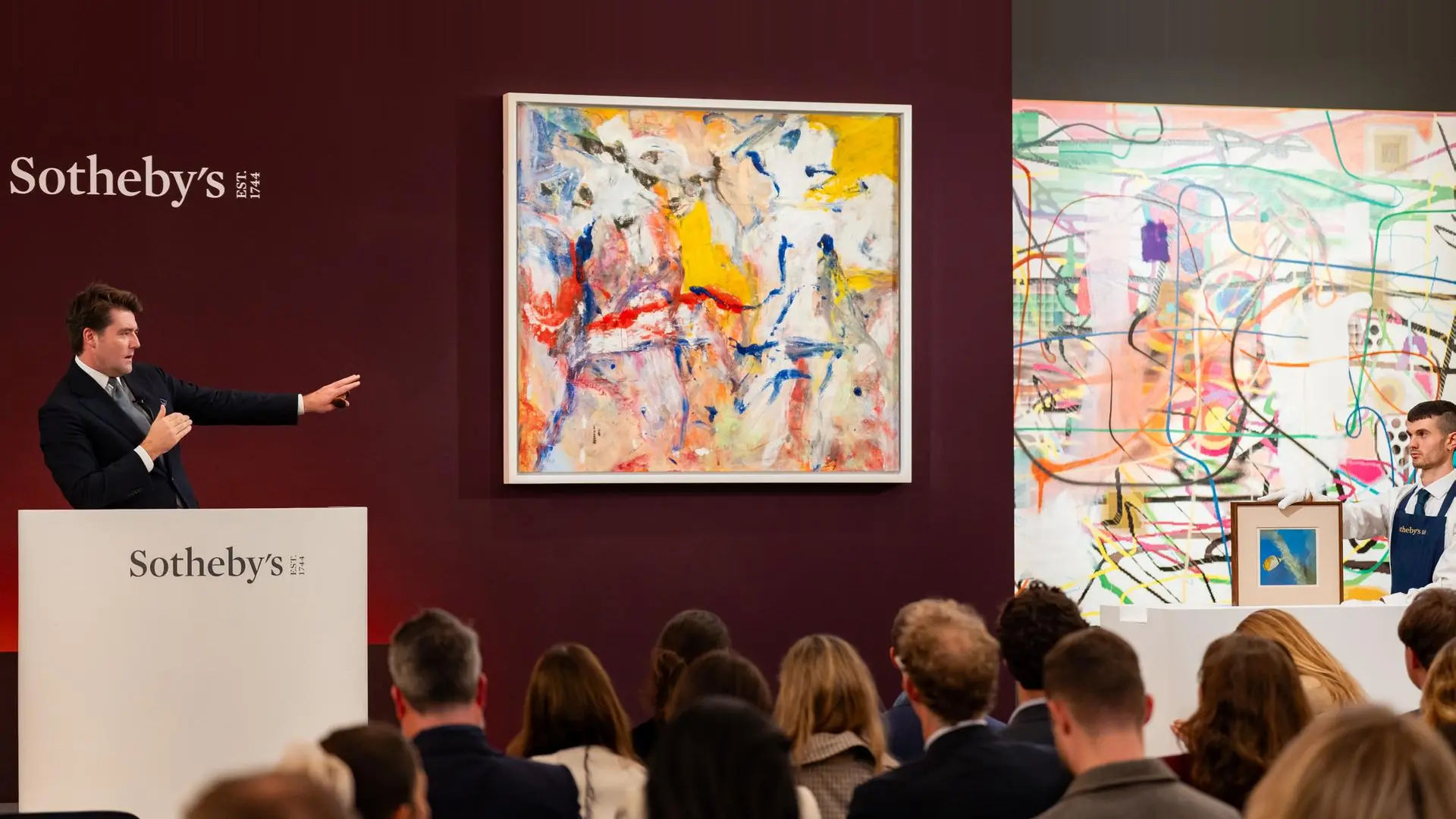 Asta d'arte Sotheby's con opere astratte e un banditore che indica.