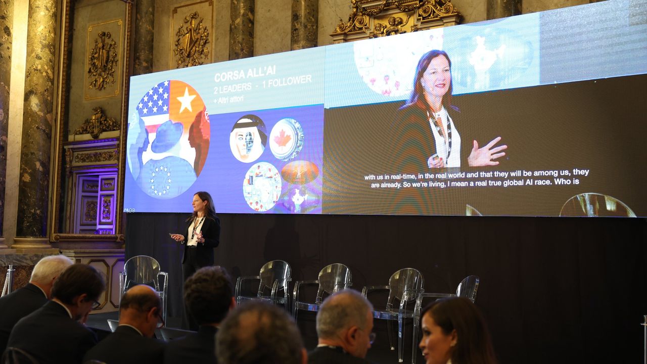 Donna parla a un pubblico durante una presentazione sull'IA, con grafiche di bandiere e volti.