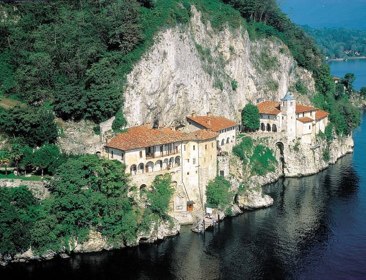 Monastero a picco sul lago, con edifici storici e vegetazione lussureggiante.