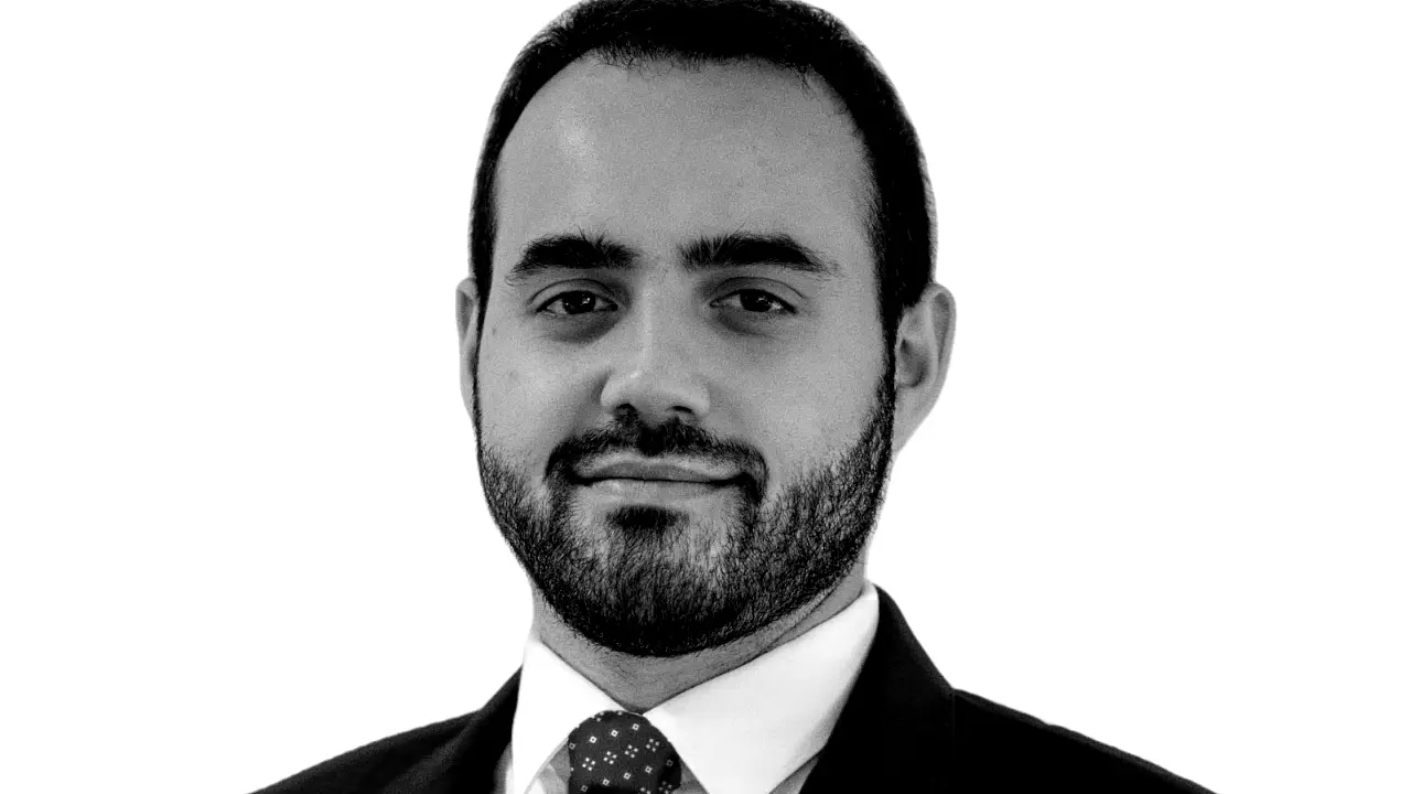 Ritratto in bianco e nero di un uomo con barba, indossa una camicia bianca e una cravatta a pois.