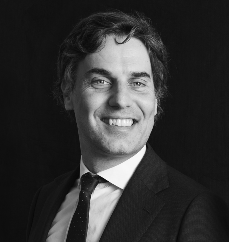 Uomo sorridente in abito scuro, camicia bianca e cravatta a pois.