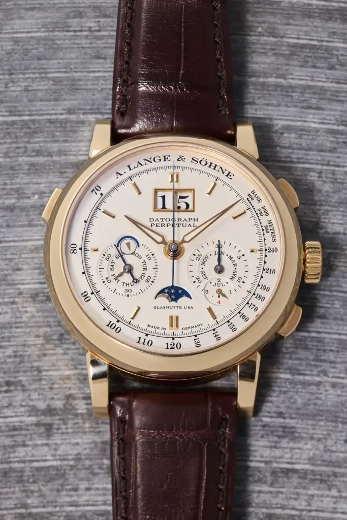 Orologio da polso in oro giallo con quadrante bianco, datario, fasi lunari e cinturino in pelle marrone.