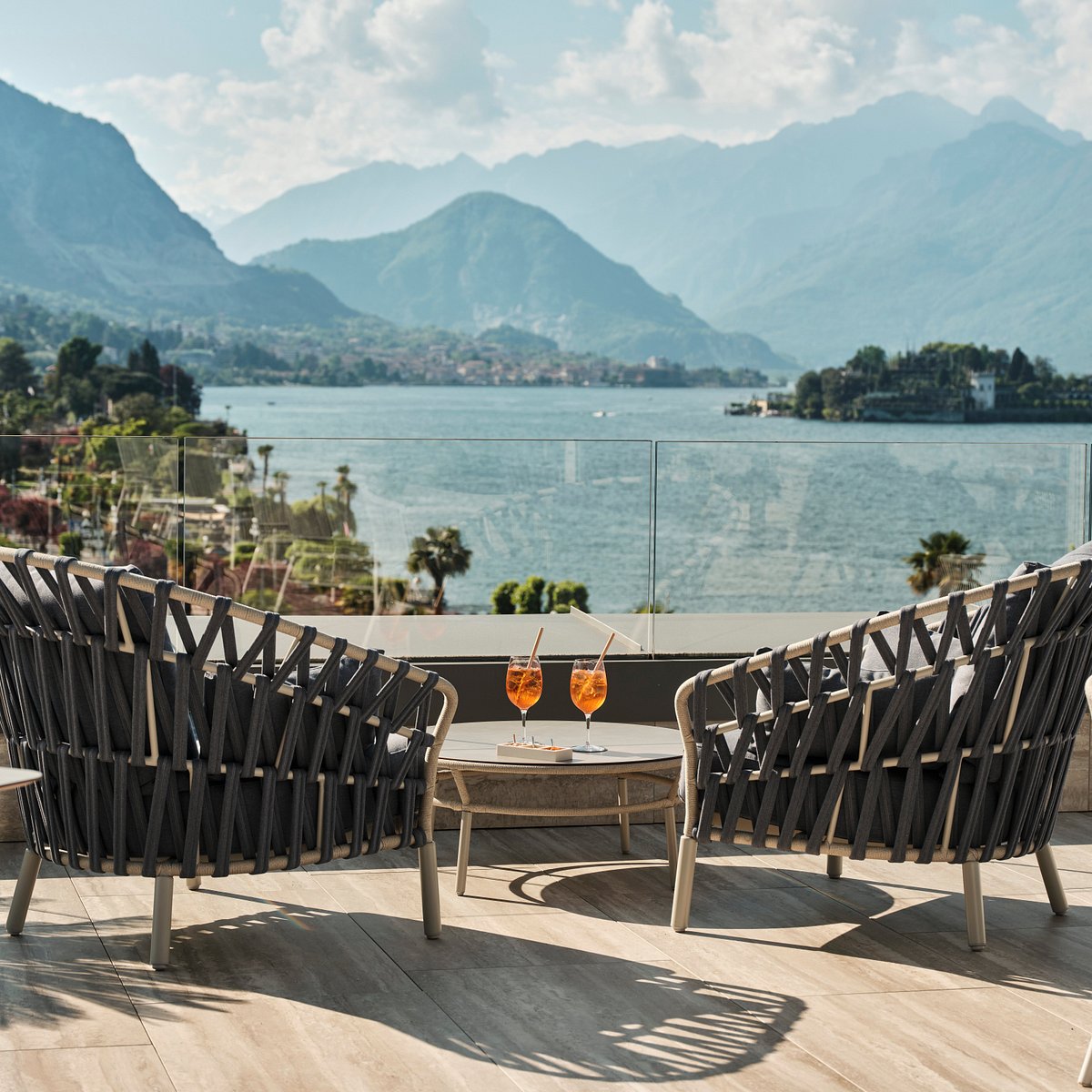 Due poltrone e un tavolino con aperitivi su un terrazzo con vista lago e montagne.