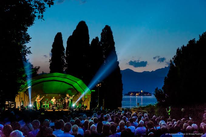 Concerto serale all'aperto con band su palco illuminato e pubblico numeroso.