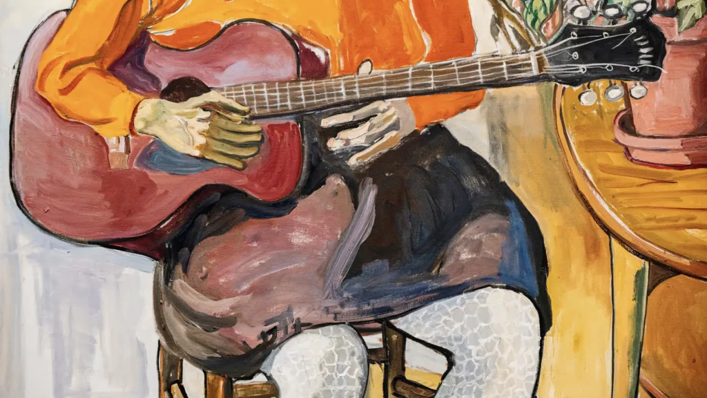 Persona con maglione arancione suona una chitarra rossa, seduta su una sedia.